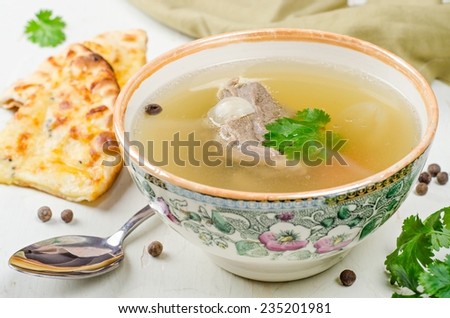 Broth with beef in bowl on white wooden table
