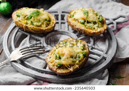 Baked stuffed potatoes with salmon, green pies and cheese on iron support and wooden background. Vintage