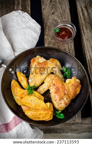 Roasted chicken wings with potatoes in iron pot on wooden vintage background