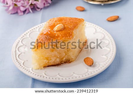 Basbousa (namoora) - arabian semolina cake with almonds and honey syrup in white plate on blue cotton background