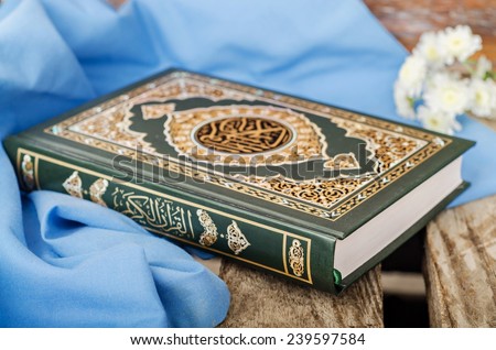 Quran - holly book of islam with spring flowers and blue scarf on wooden background. Selective focus on book