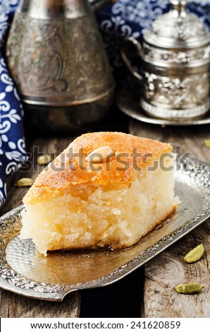 Basbousa (namoora) - arabian semolina cake with almond and honey syrup in iron tray on wooden background. Slice of cake