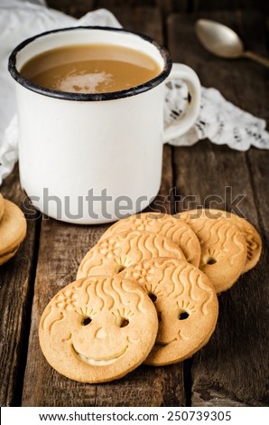 Smiling cookies near vintage white cup and napkin on dark wooden background. Selective focus