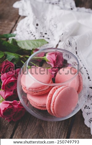 Pink Macaroons in glass bowl with roses on wooden vintage background. Selective focus. Toned image