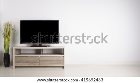 Television put on wood table, background white wall.