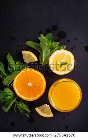 Fresh orange juice, orange and lemon slices, mint leaves and ice on dark background, top view