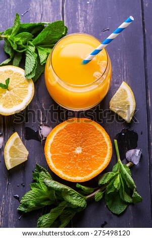 Fresh orange juice, orange and lemon slices, mint leaves and ice on dark background, top view. Selective focus