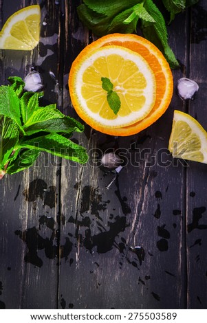 Orange and lemon slices with mint and ice cubes on grunge black wooden background. Top view. Selective focus