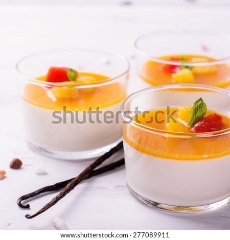 Dessert panna cotta with fresh berries and vanilla pods on wooden background, selective focus. Square image