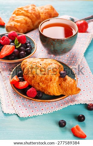 Delicious breakfast with fresh almond croissants, berries and cup of tea on sky-blue wooden background, selective focus