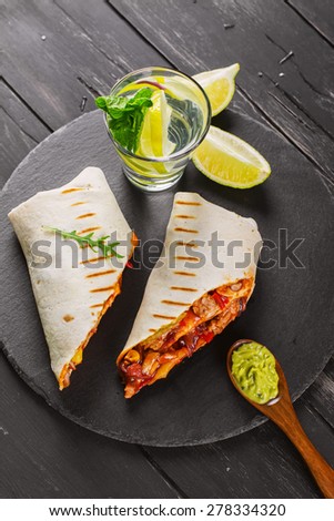 Tasty fast food: mexican burritos with guacamole sauce on black wooden background, selective focus