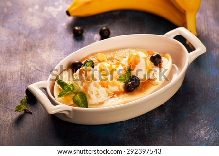 Delicious banana split with blueberry, mint, almonds and sauce on blue wooden background. Selective focus. Toned image
