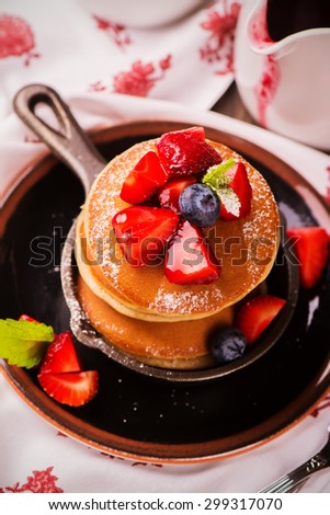 Stack of pancakes with fresh strawberry, honey and mint in frying pan on wooden rustic background. Selective focus