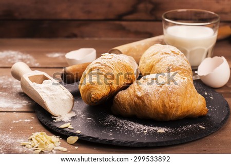 Fresh baked croissants with almond leaves on the wooden table. Selective focus