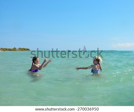 Sisters playing ball in the green beautiful ocean, blue sky in the background, Florida