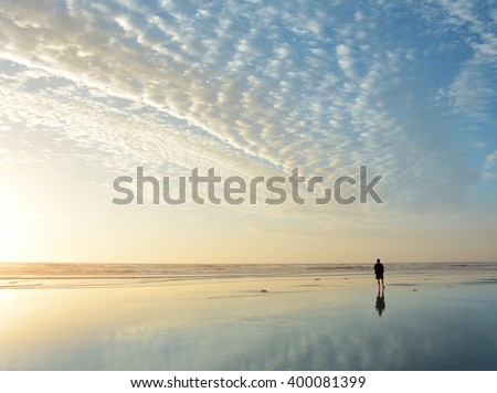 Man walking on beach at sunrise, beautiful cloudy sky reflected on the beach, Jacksonville, Florida, USA.