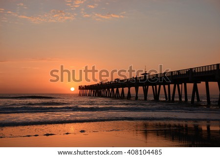 Sun rising over horizon and pier, beach illuminated with sunlight, Jacksonville Florida, USA.