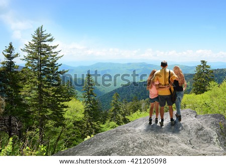 Family hiking on vacation, standing with arms around on top of the mountain, looking at beautiful summer mountains landscape. Blue sky in the background. Copy space. North Carolina, USA.