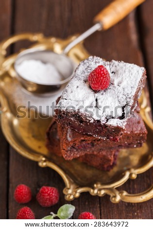 Chocolate brownie with raspberries, sprinkled with powdered sugar.