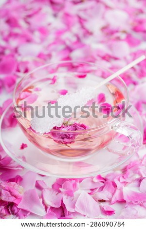 Tea with rose petals in a glass Cup with sugar crystals on the shelf. Rose water.