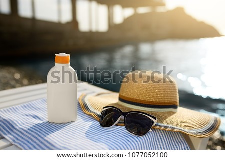 Suntan cream bottle and sunglasses on beach towel with sea shore on background. Sunscreen on deck chair outdoors on sunrise or sunset. Skin care and protection concept. Golden tan.