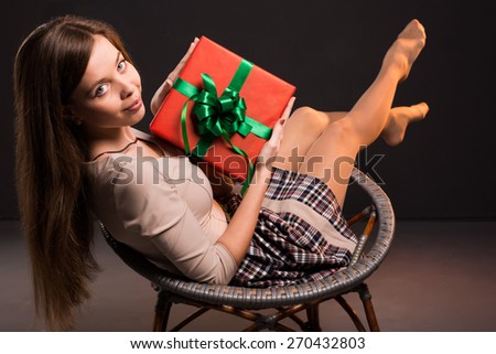 Photo of a pretty sensual girl on a crocheted chair with a gift in her hands on a dark background