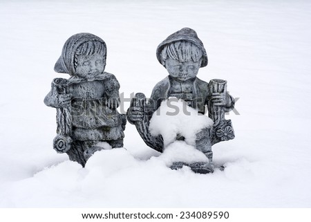 Cute little boy and girl concrete sculpture statue siting in the garden during first Snow