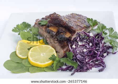 Smoked Barbecue Baby Back Ribs decorated with Spinach Red Cabbage Lemon and Parsley in a White Ceramic Plate
