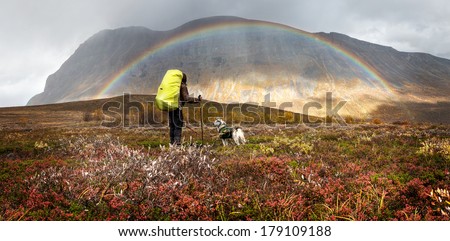 Hiker with dog, backpack and rainbow on a rainy day
