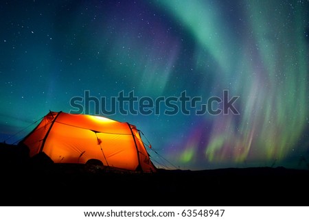 Northern lights over a illuminated tent in Lapland
