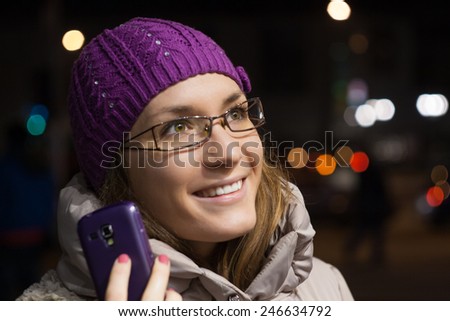 Woman wearing winter clothes using smart phone in the city by night