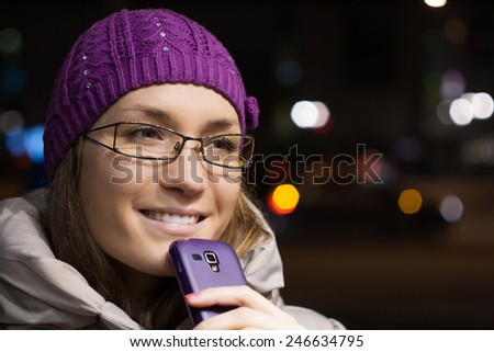 Woman wearing winter clothes using smart phone in the city by night
