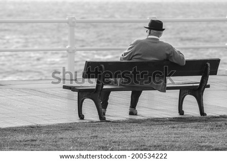 Old man sitting on a bench facing the sea