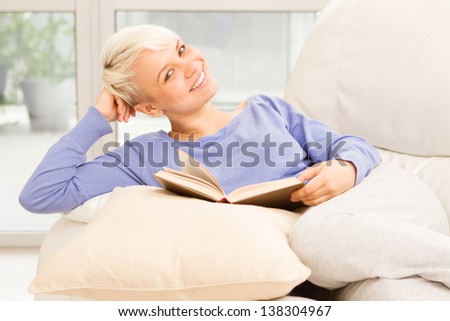 Photo of pretty smiling woman with the book on the sofa