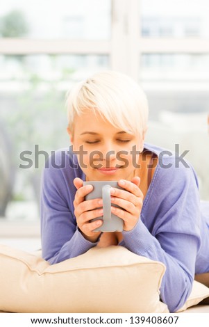 Photo of pretty woman with mug on the floor laying on a pillow