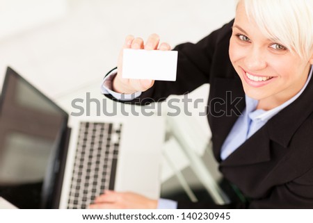 Photo of businesswoman holding business card while smiling next to her notebook