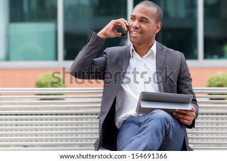 Smiling Afro American Manager Sitting On A Bench And Phoning