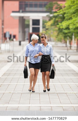 Two businesswoman are walking on the street while talking and laughing