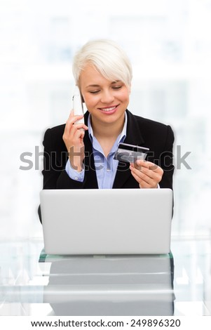 photo blonde smiling woman speaking at phone while online shopping with credit card in office