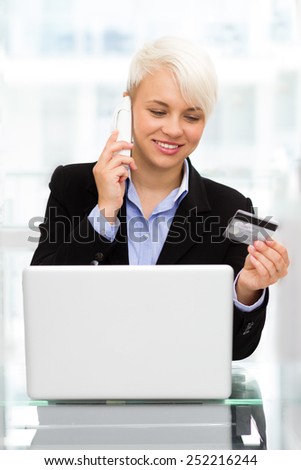 photo blonde smiling woman speaking at phone while online shopping with credit card in office