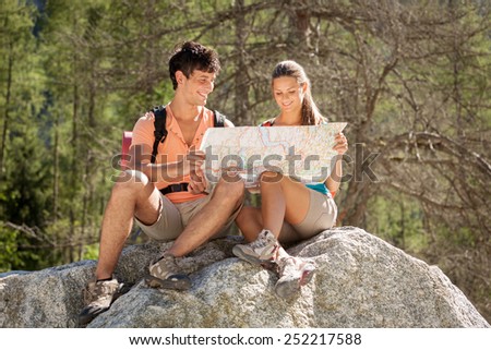 Photo of young caucasian couple looking at the path on a map while relaxing on a big rock
