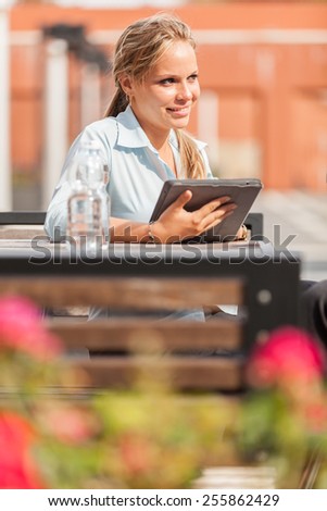 Photo of attractive smiling businesswoman with tablet pc siting outdoor and looking around