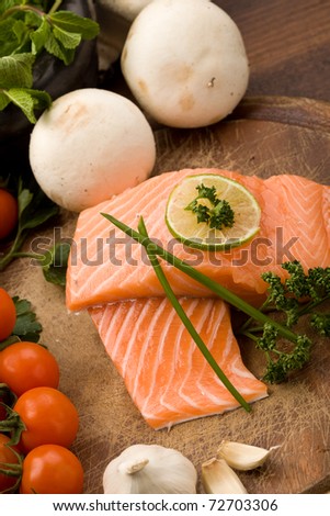 photo of delicious salmon filet with lime and parsley on chopping board with vegetables arround