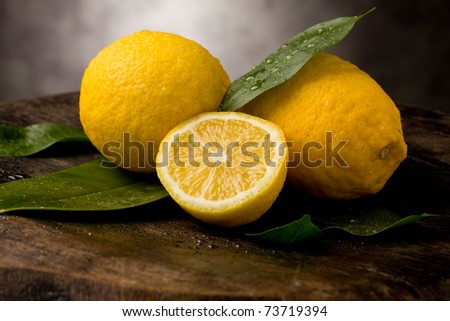 fresh yellow lemons with leaves and water drops on wooden table