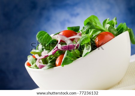 Colorful mixed salad inside a bowl on white towel in front of blue background