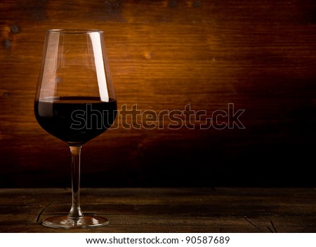 photo of delicious dark red wine goblet on wooden table illuminated by spot