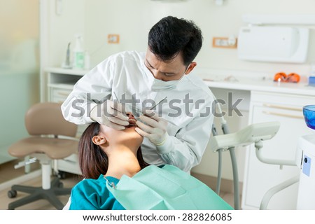 photo of male asian dentist diong a dental check up to a young asian woman in a dentist office