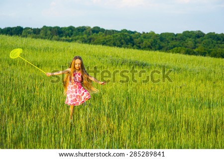 Girl with a butterfly net runs on a glade. Little girl playing in the grass.