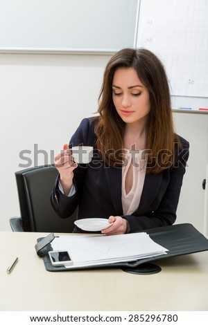 Business woman in the office. Secretary drinking coffee in the workplace.