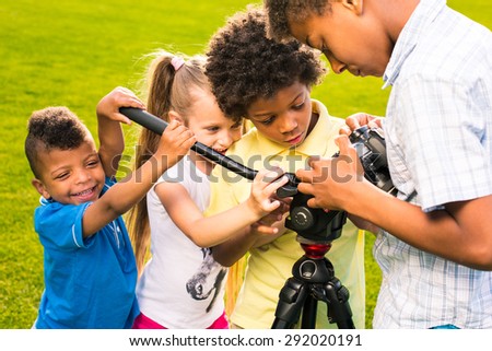 Four nice children are playing with camera and going to take a picture.